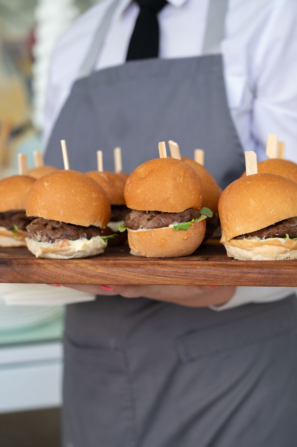 Four identical beef sliders on brioche buns arranged in a row on a wooden serving board.