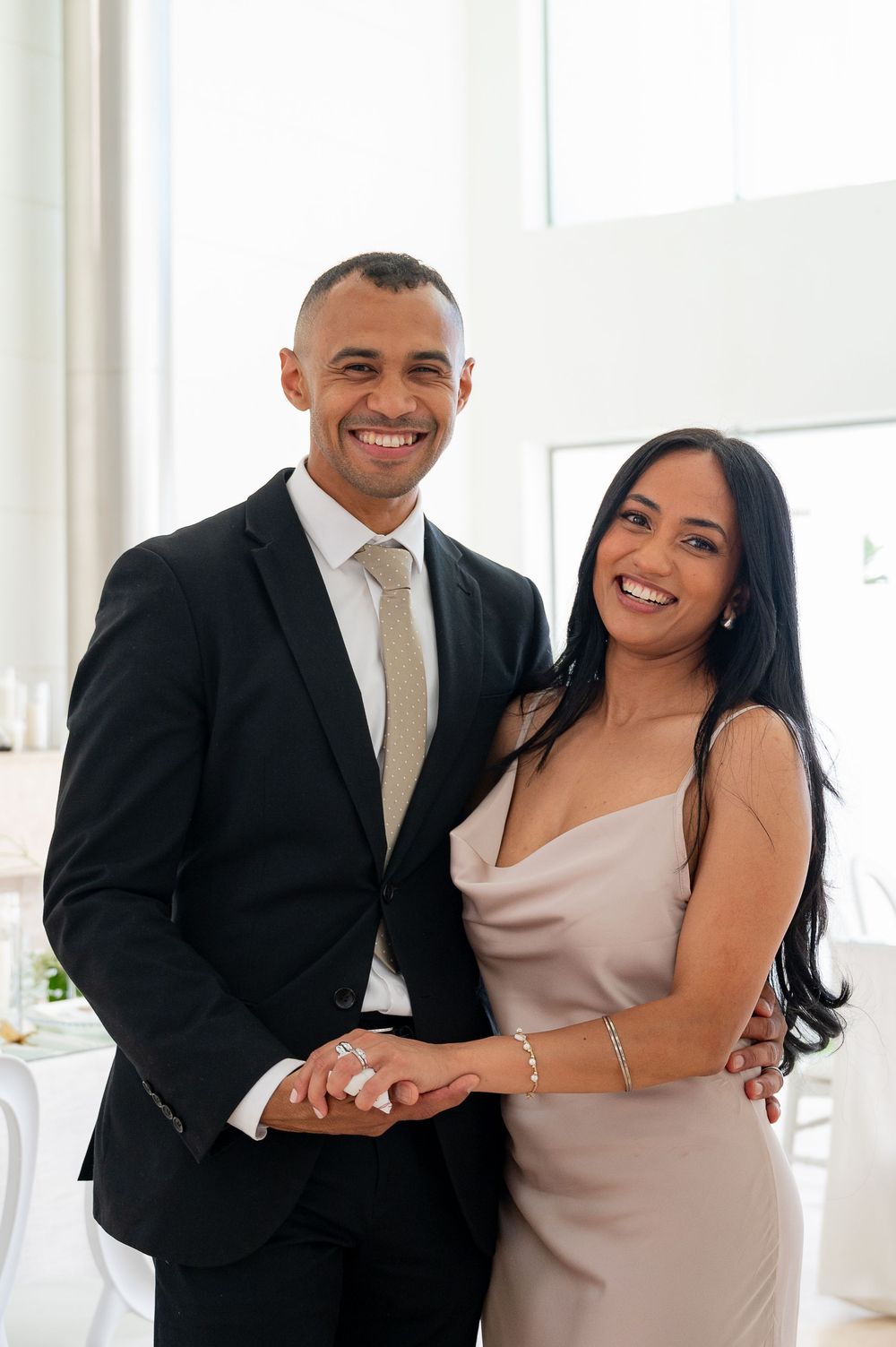 A couple in formal attire sharing joyful moments together in a bright interior space.