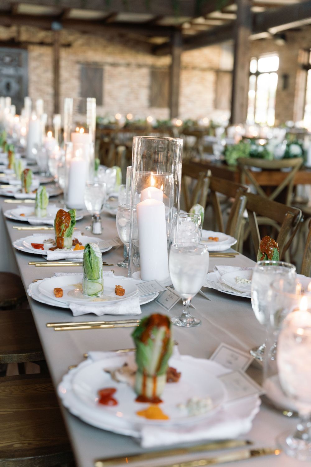Elegant table setting with glass candle holders and green garnishes on white plates.