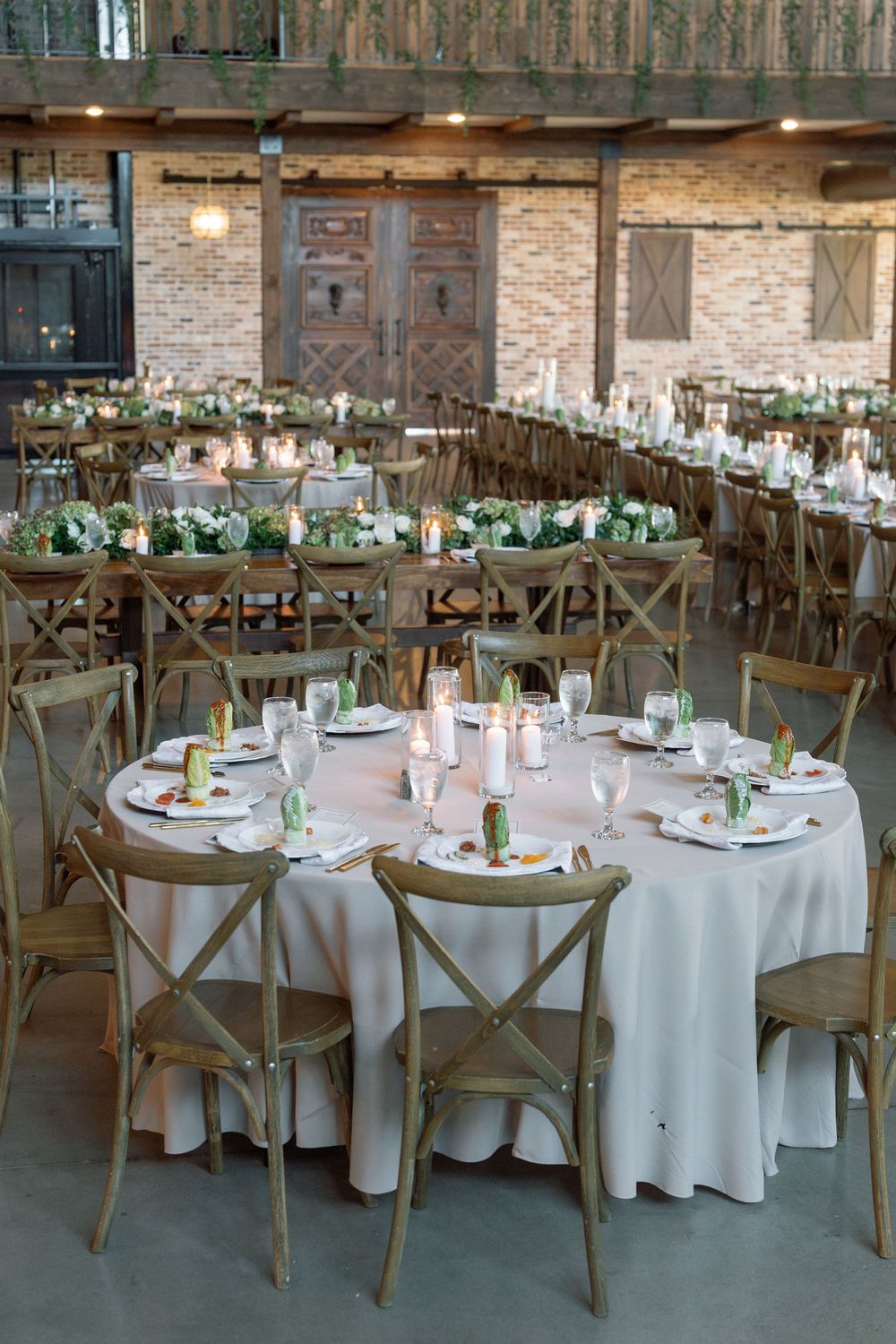 Elegant wedding reception venue with round tables, white linens and wooden crossback chairs.