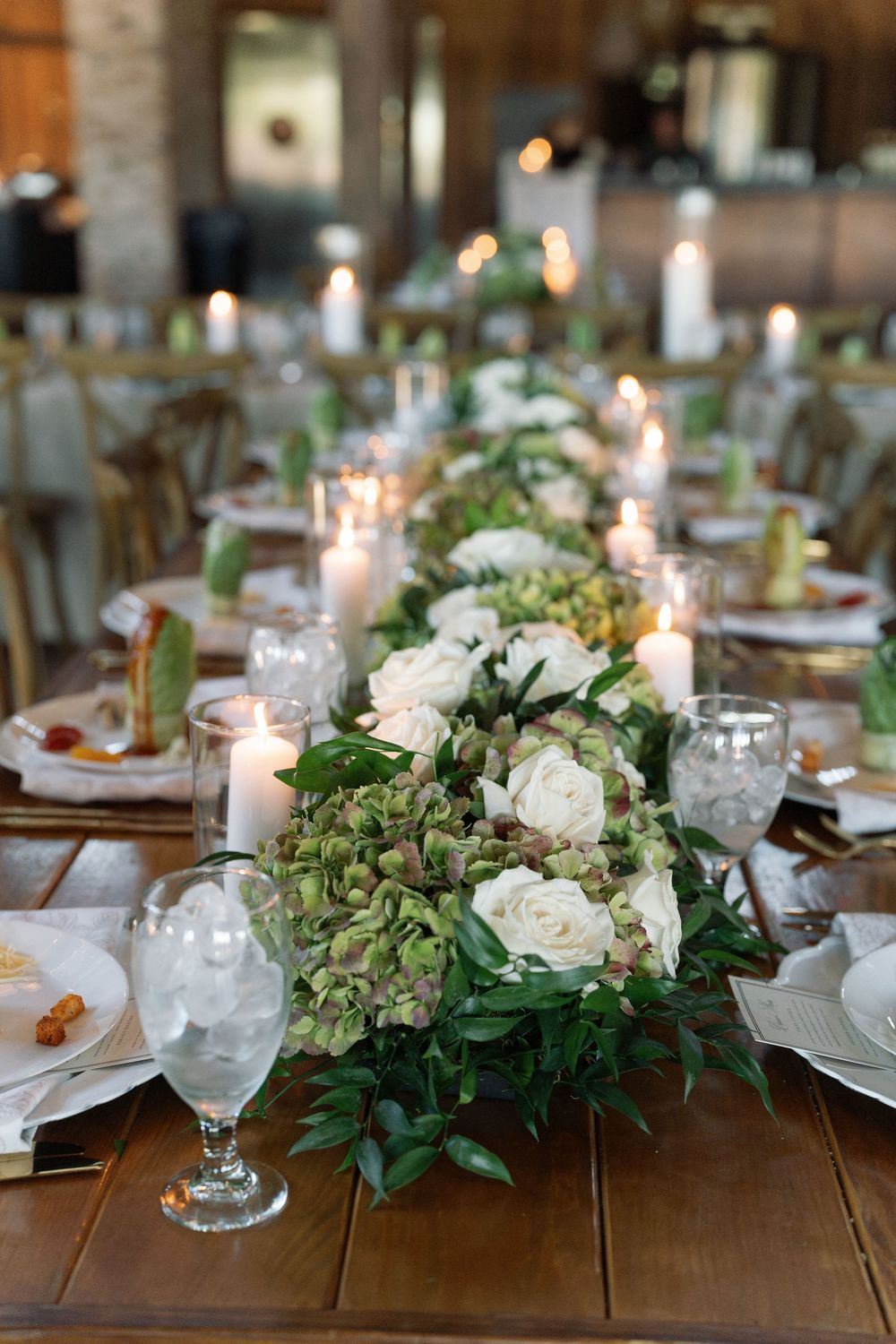 Romantic wedding table setting with white roses, greenery centerpieces and glowing candles.