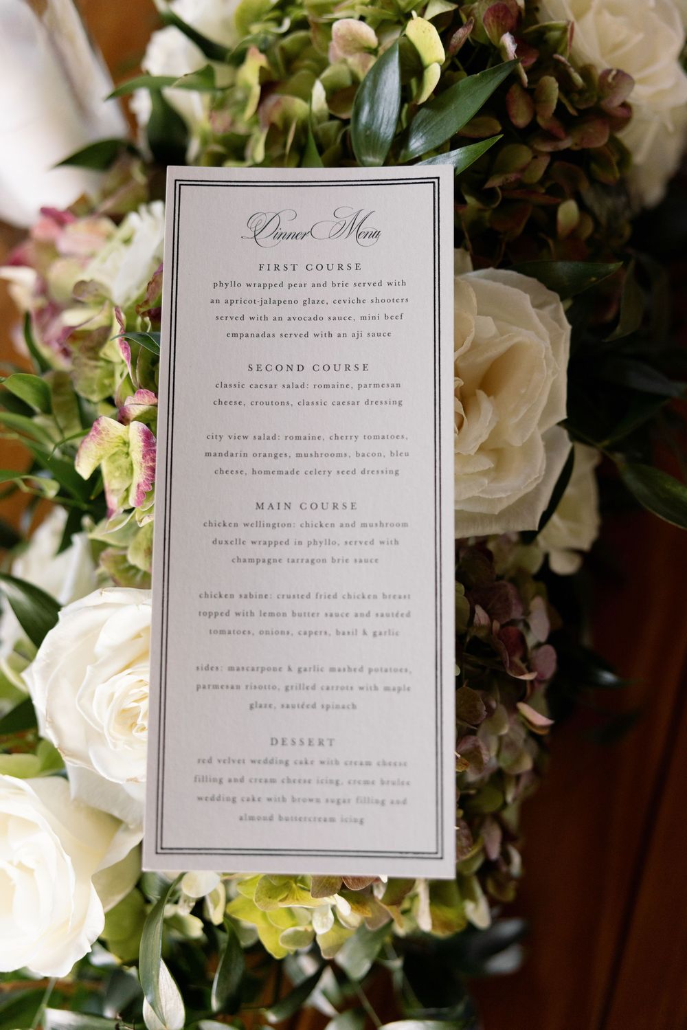 Elegant dinner menu card nestled among white roses and greenery.