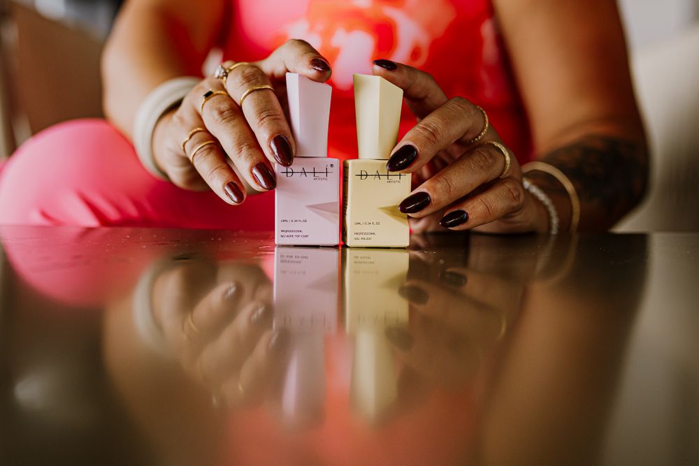 Two hands holds two nail polish products on the table..