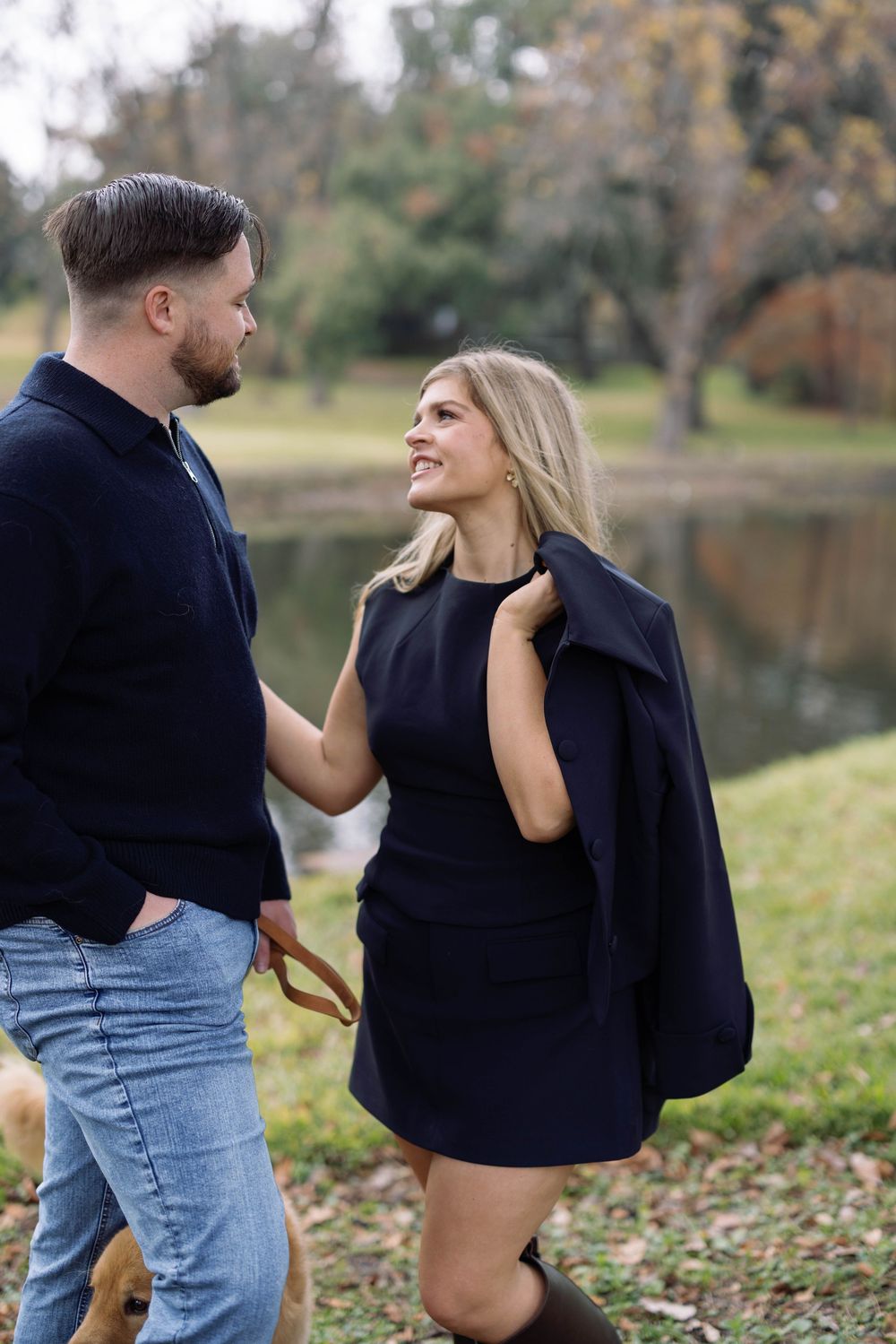 Young couple in casual attire dance together on fallen autumn leaves near a lakeside.