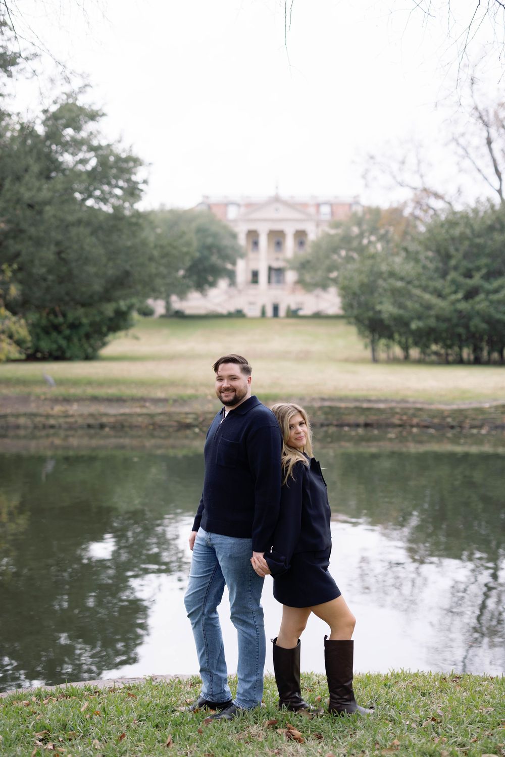 A couple sitting together by a tranquil pond surrounded by green grass and trees on a peaceful day.