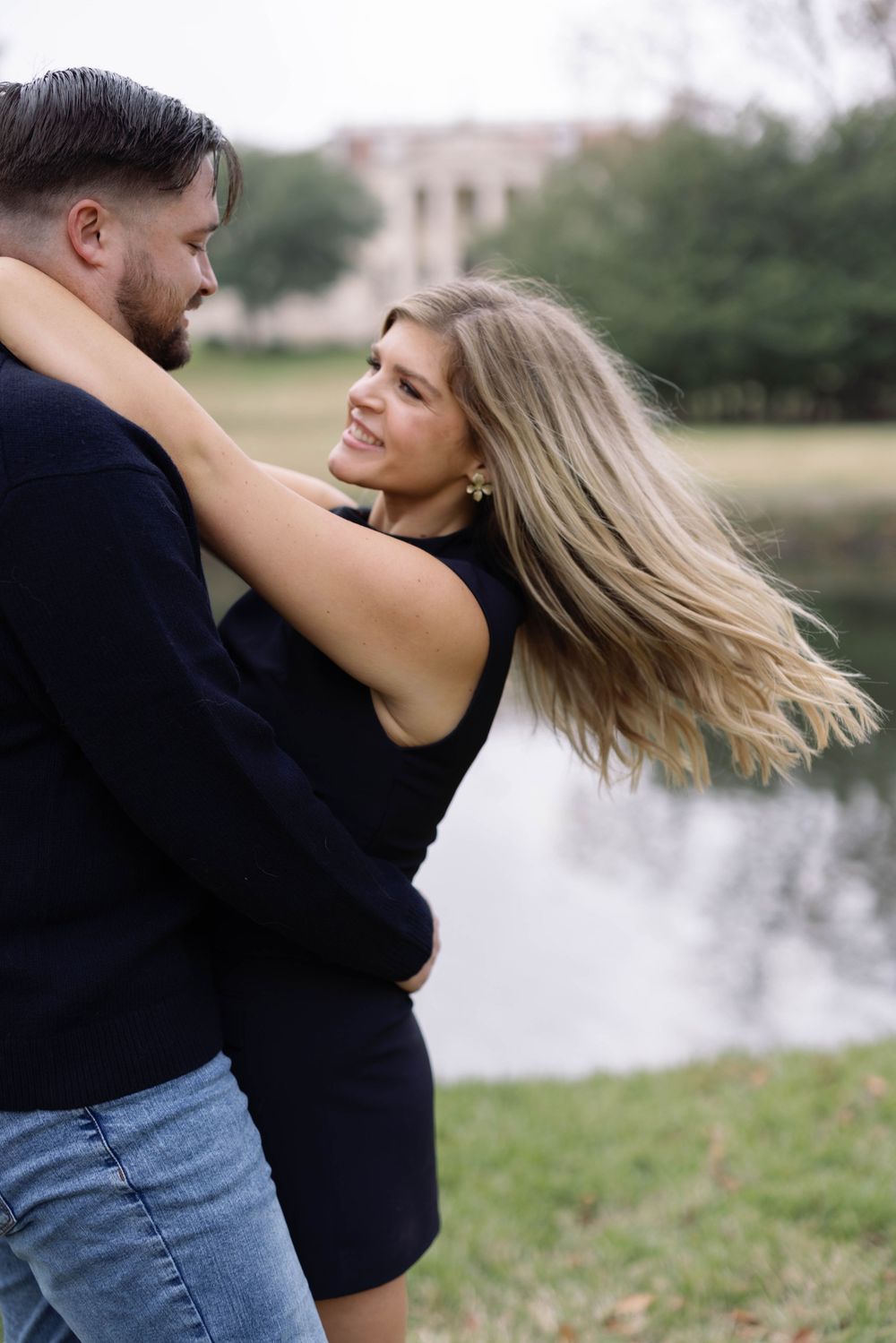 A romantic couple embracing and laughing together by a lake on an autumn day.