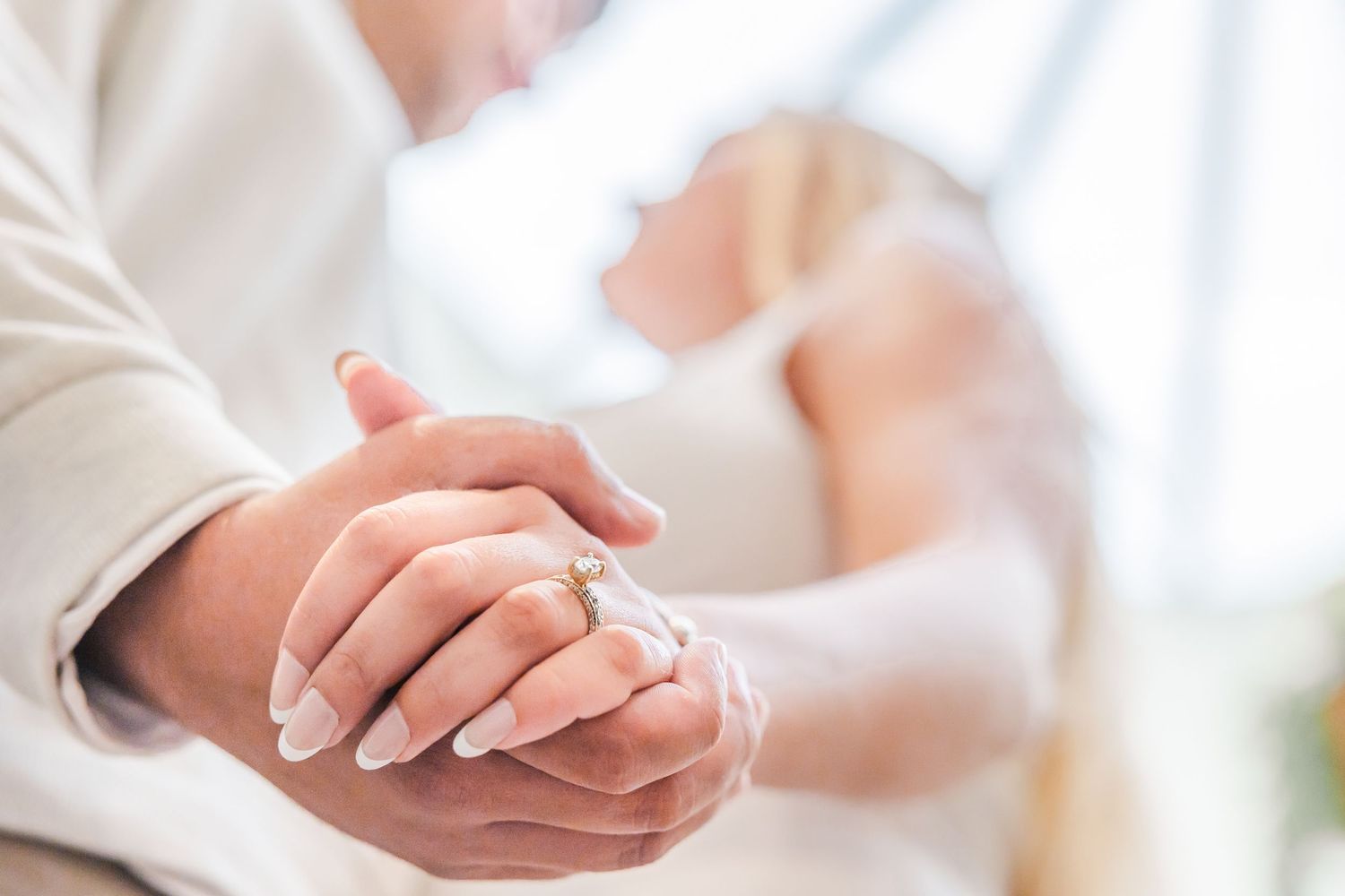 Two hands clasp together tenderly in a loving gesture, with soft natural lighting in the background.