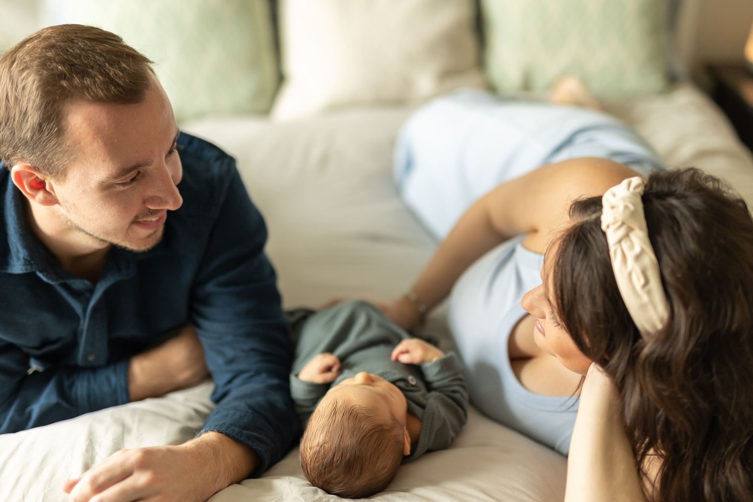 New parents on their bed smiling at each other as their baby rests between them
