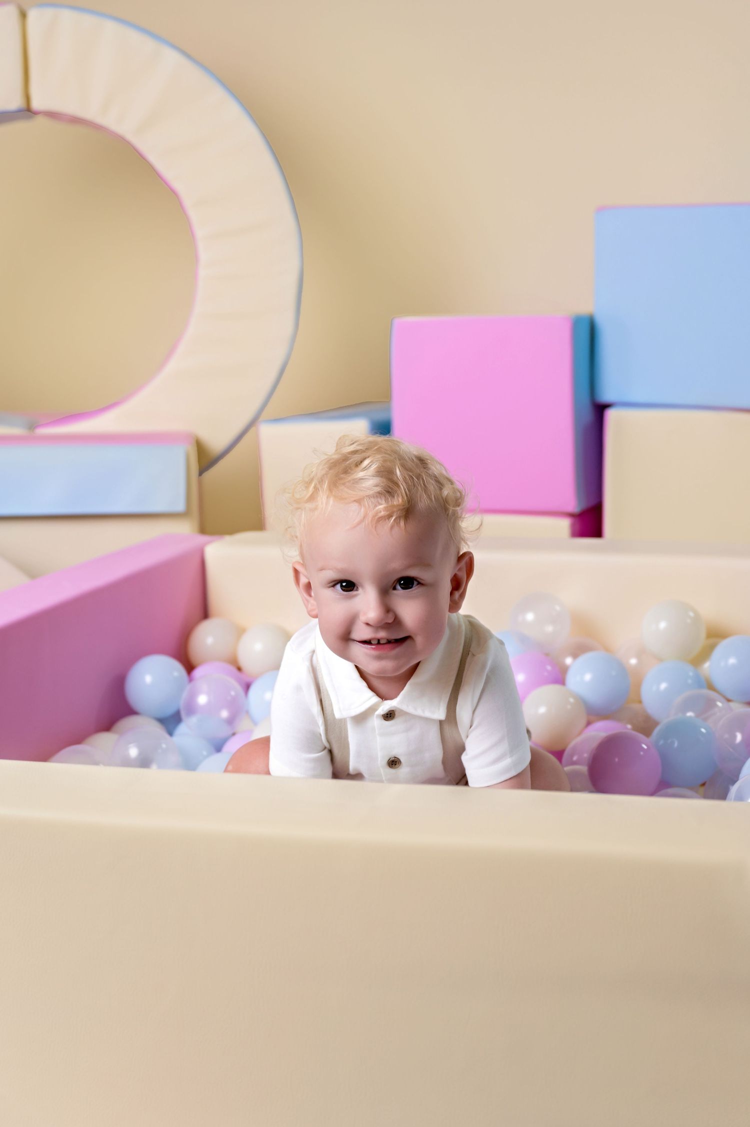 Baby boy smiling in pastel soft play ball pit during a photoshoot in Haverhill, Suffolk.