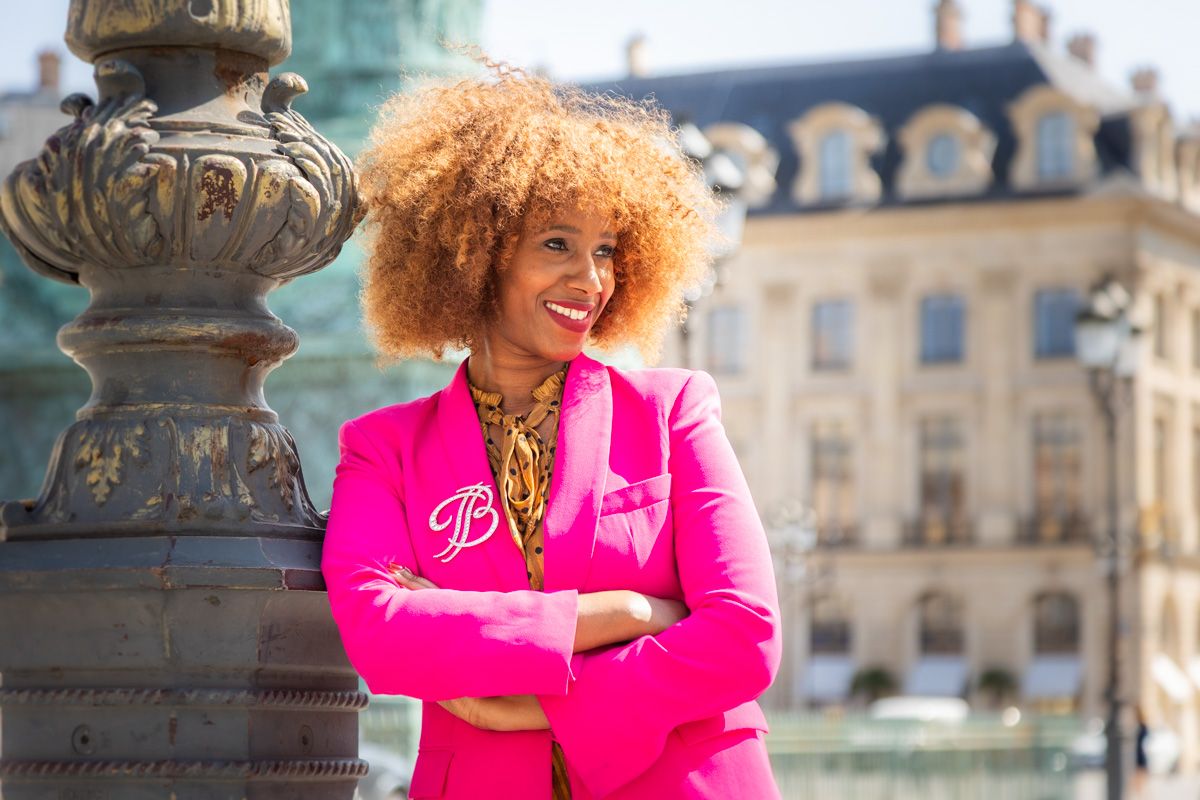 Stylish person wearing bright pink blazer with natural curly hair poses near ornate stone architecture in Paris.