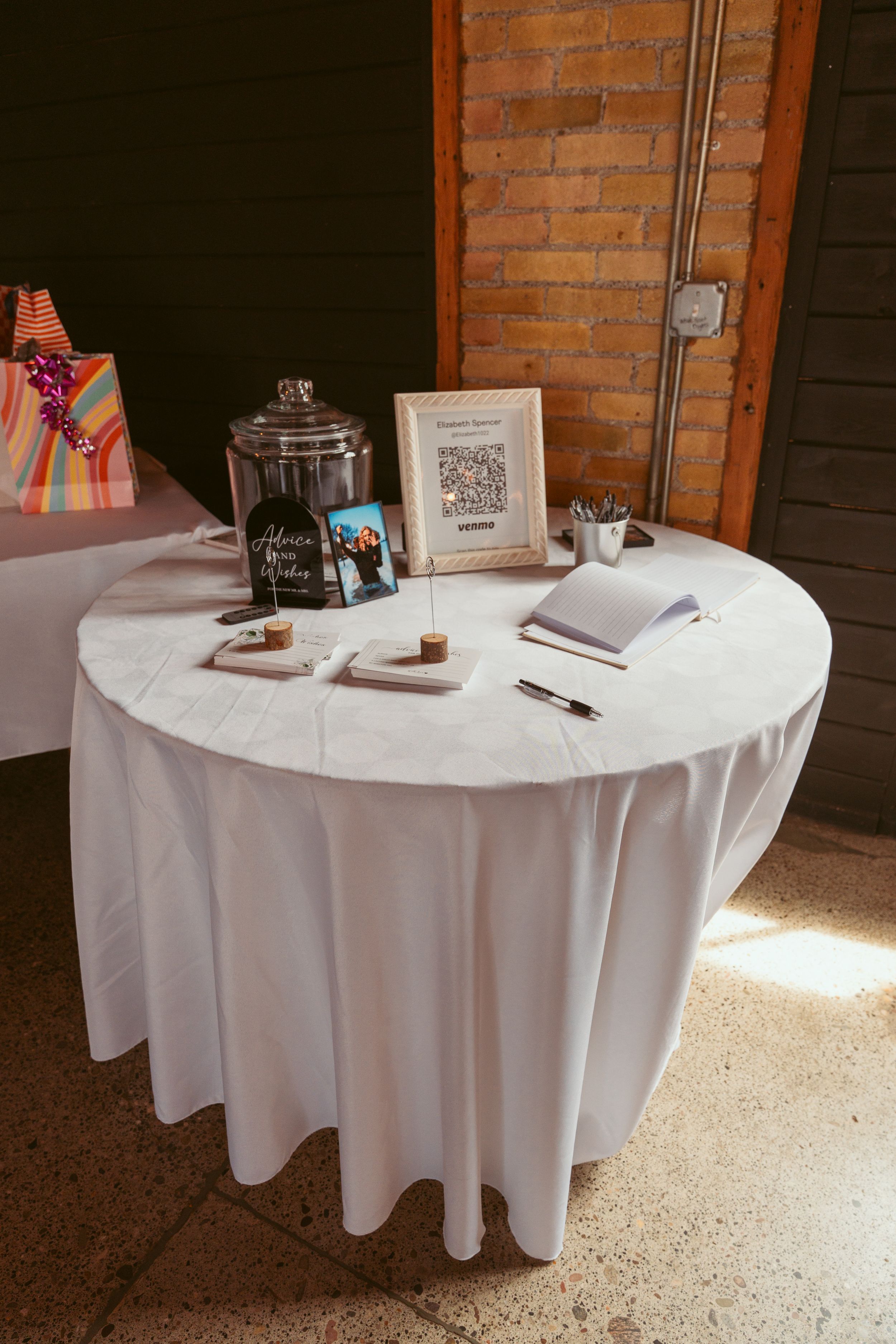 Wedding guest book and decor items arranged on a round table covered with white linen tablecloth.