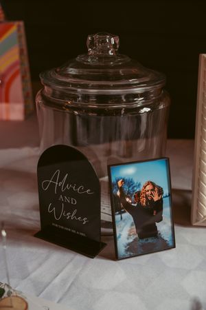 Glass cookie jar next to 'Advice and Wishes' sign and framed photo on white tablecloth.