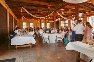 Wedding reception setup in a rustic wooden venue with white tablecloths and string lights creating a warm atmosphere.