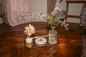 Simple wedding decor featuring dried flowers in glass vases on a dark wooden table.