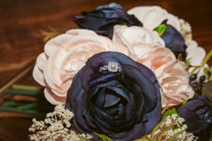 Close-up of black and peach silk roses arranged with baby's breath flowers on dark wooden surface.