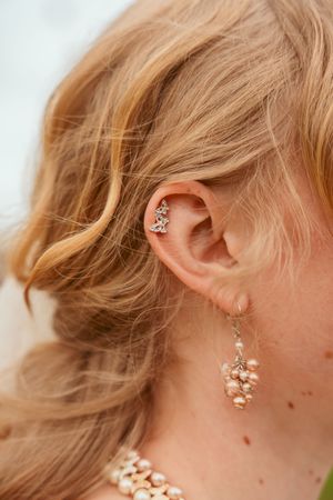 Delicate crystal ear jewelry featuring a helix piercing and dangling pearl earring against blonde hair.