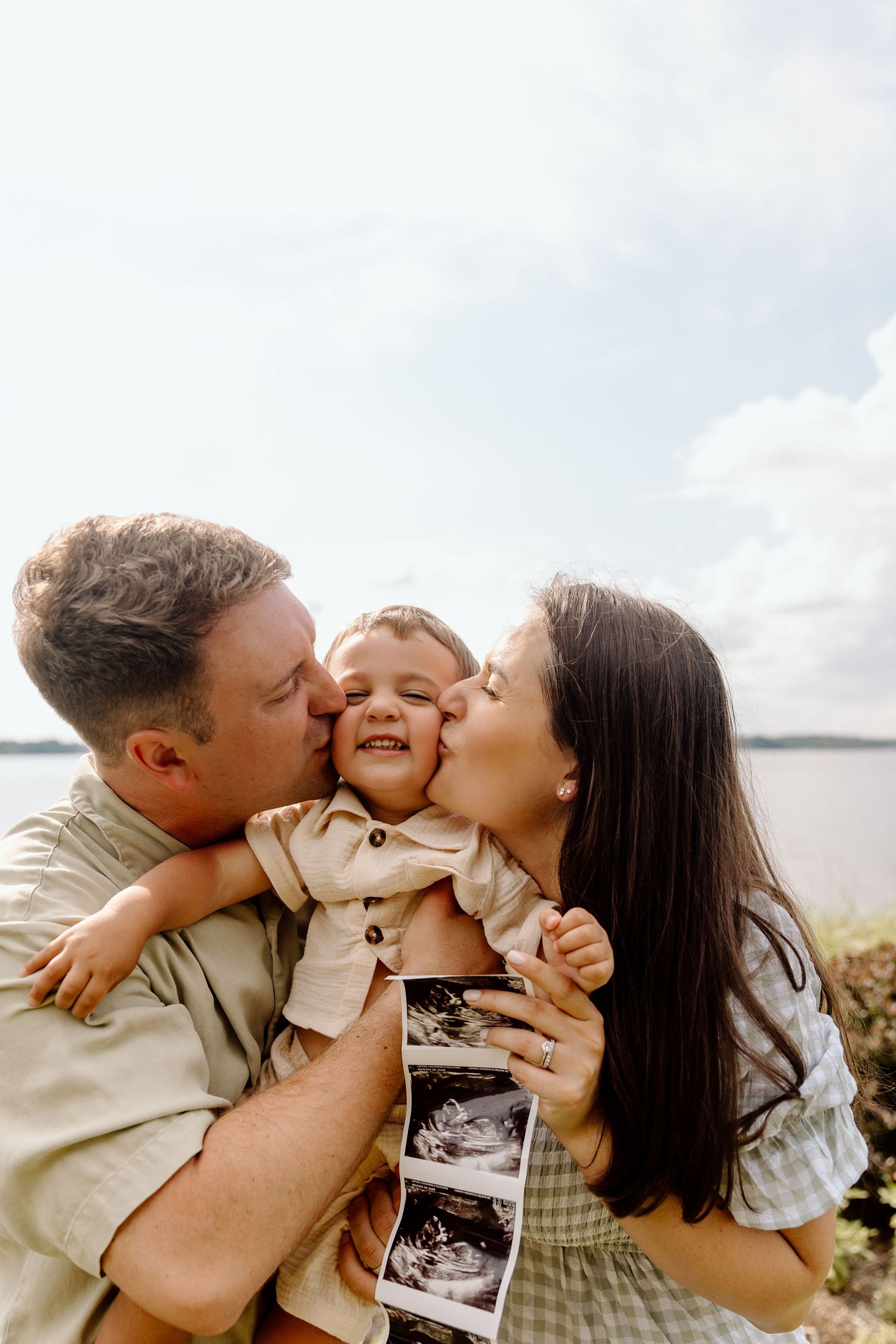 A couple shares kisses with their child while holding ultrasound photos in a heartwarming pregnancy announcement photo series.