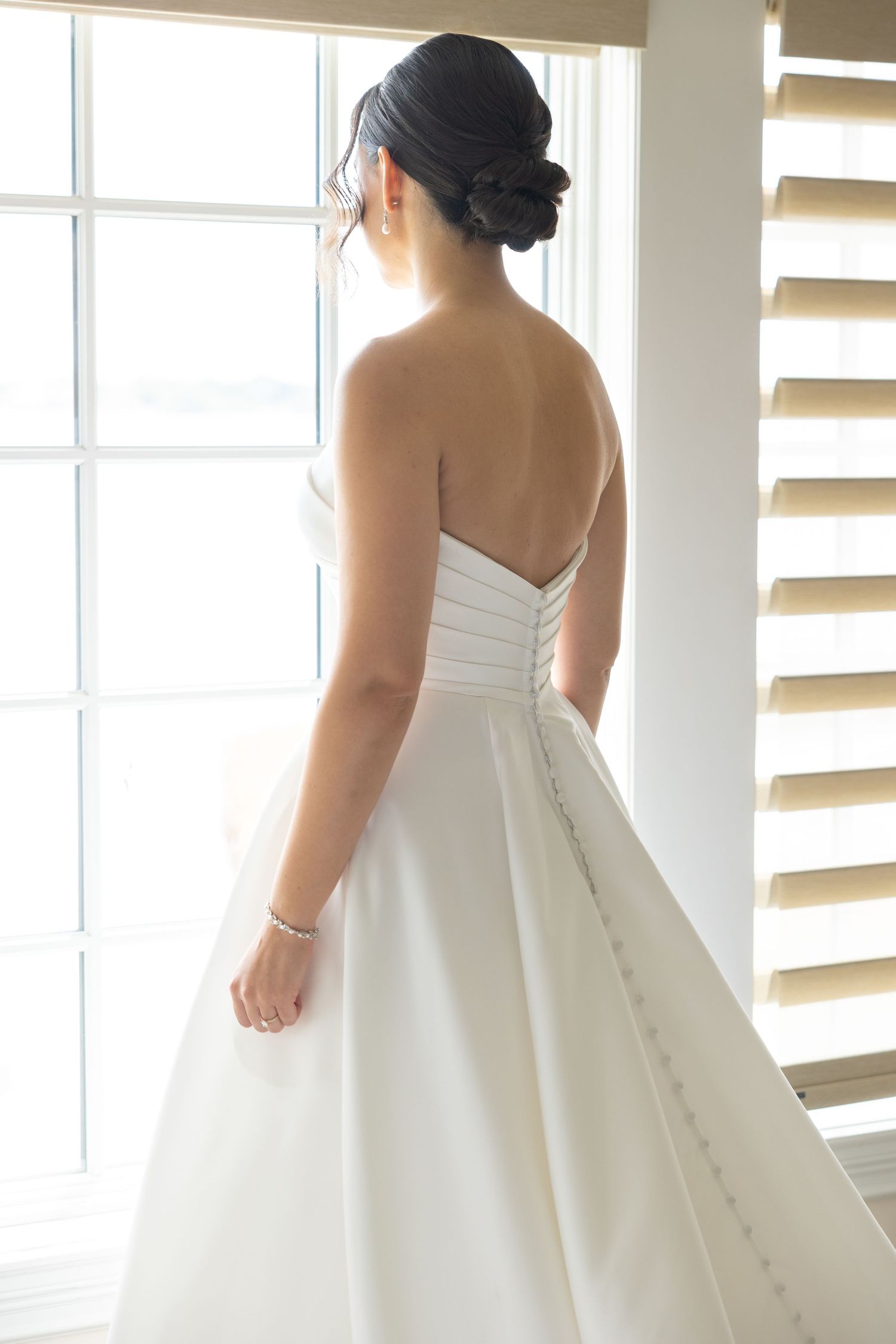 A stunning white satin wedding gown with corset back and full skirt photographed near a sunlit window.