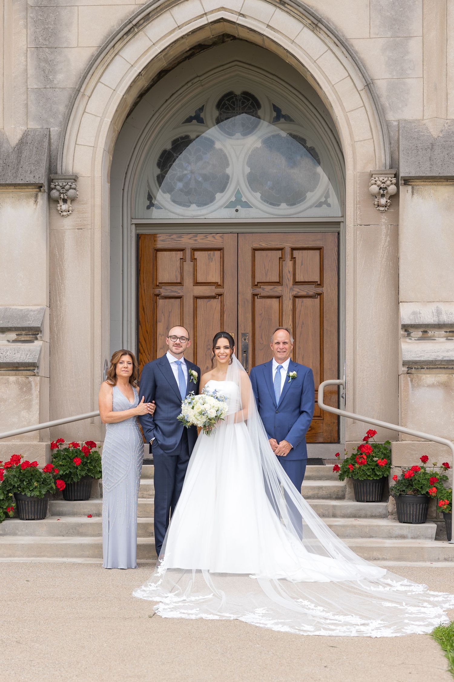 A wedding party stands outside a stone church with grand wooden doors and arched architecture. Rachel Martinez Photography Novi Michigan