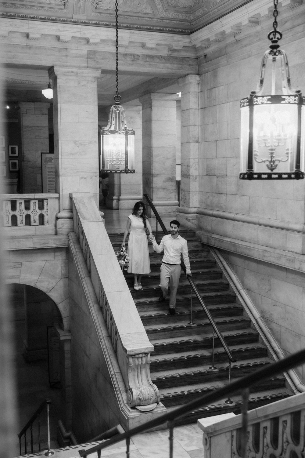 Interior view of ornate marble staircase with vintage pendant lighting in historic building entrance hall.