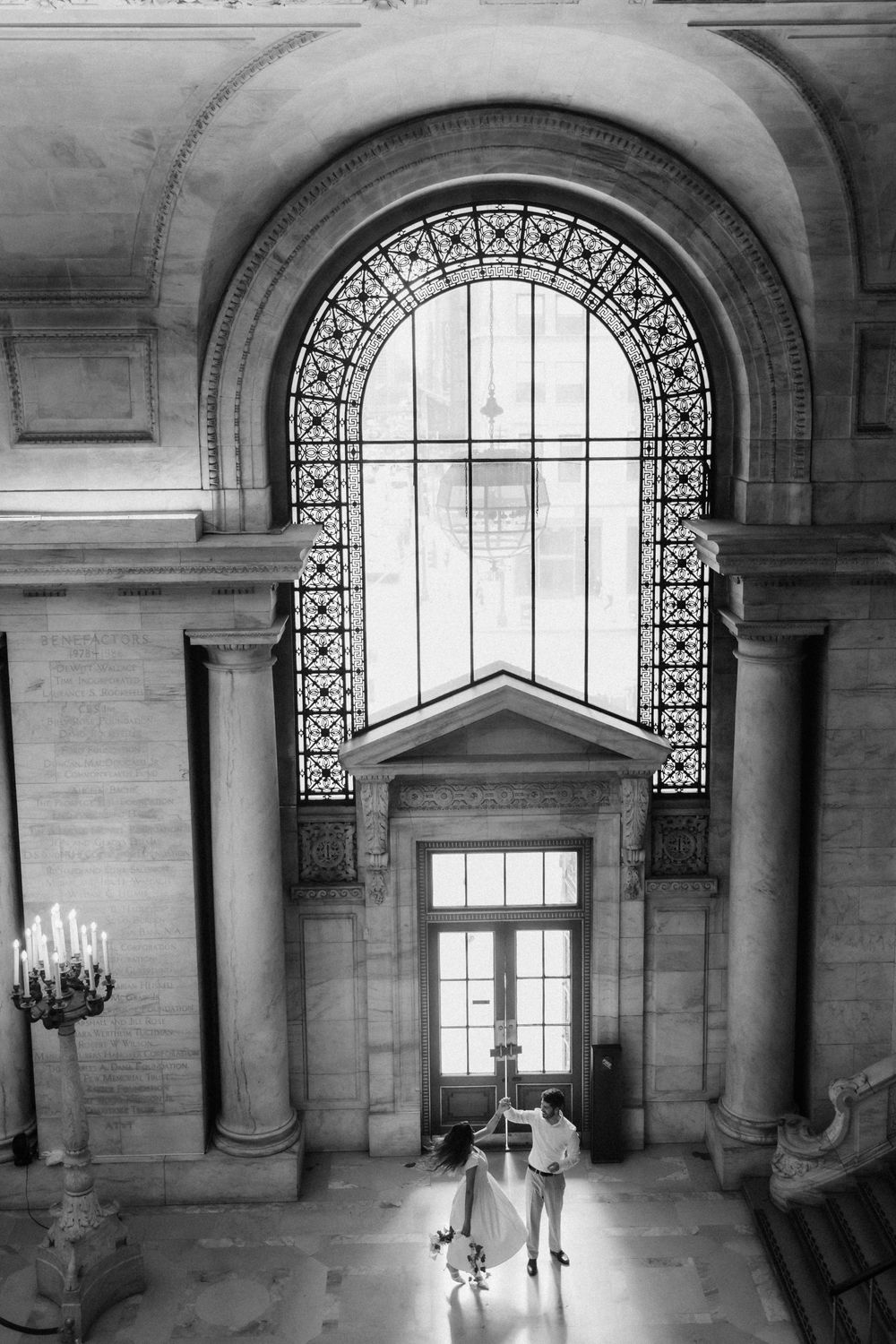 Bright, airy architectural interior of New York Public Library showing columns and arched windows with decorative ironwork.
