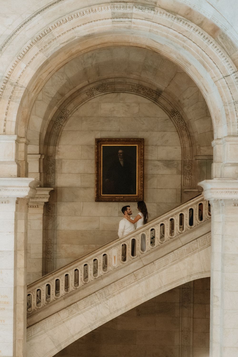 An architectural interior view of repeating stone arches and a curving staircase in a classical building.