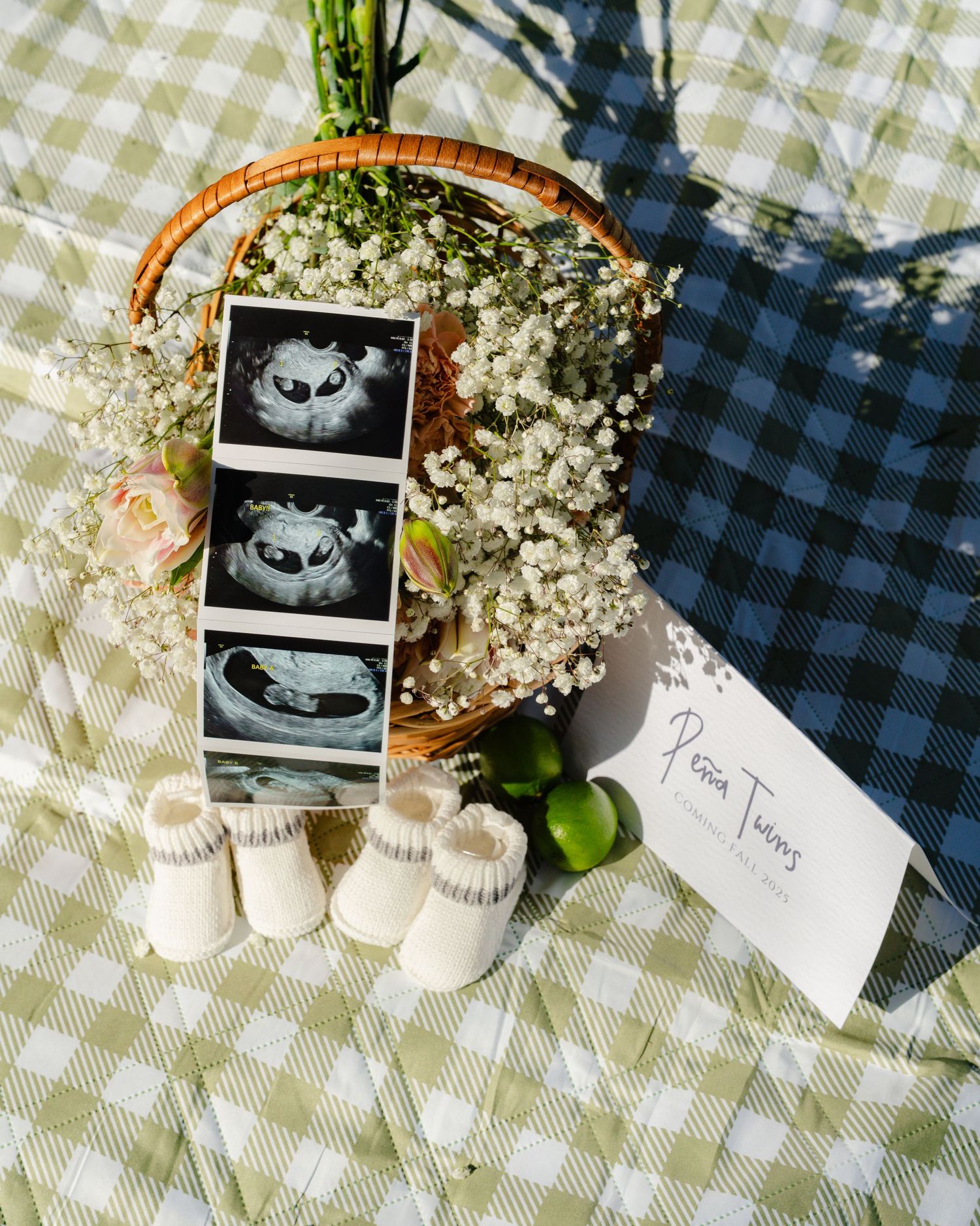 Pregnancy announcement setup with ultrasound photos and baby shoes on a gingham picnic blanket.