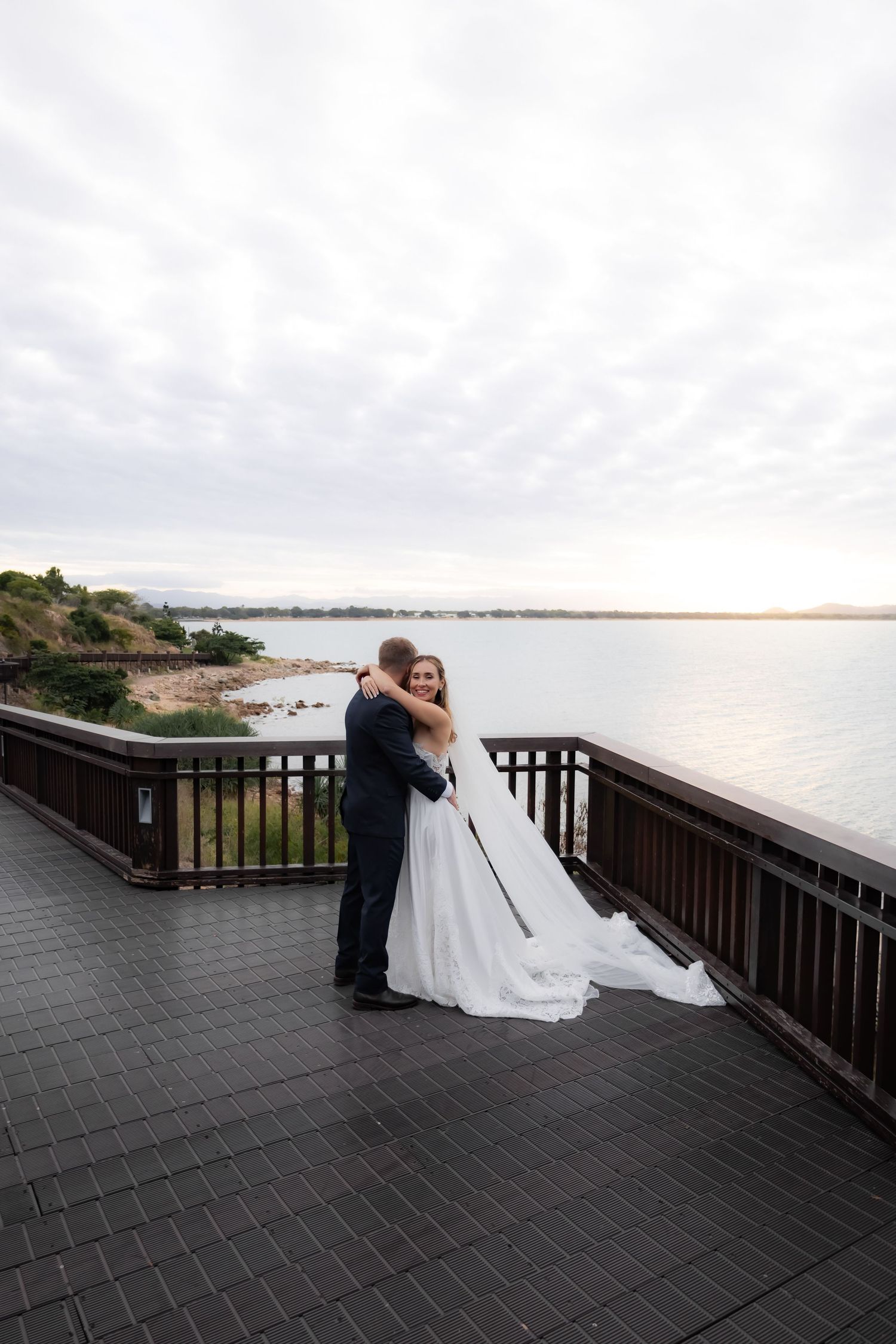 Newlyweds share tender moments on a seaside deck during their wedding photoshoot.