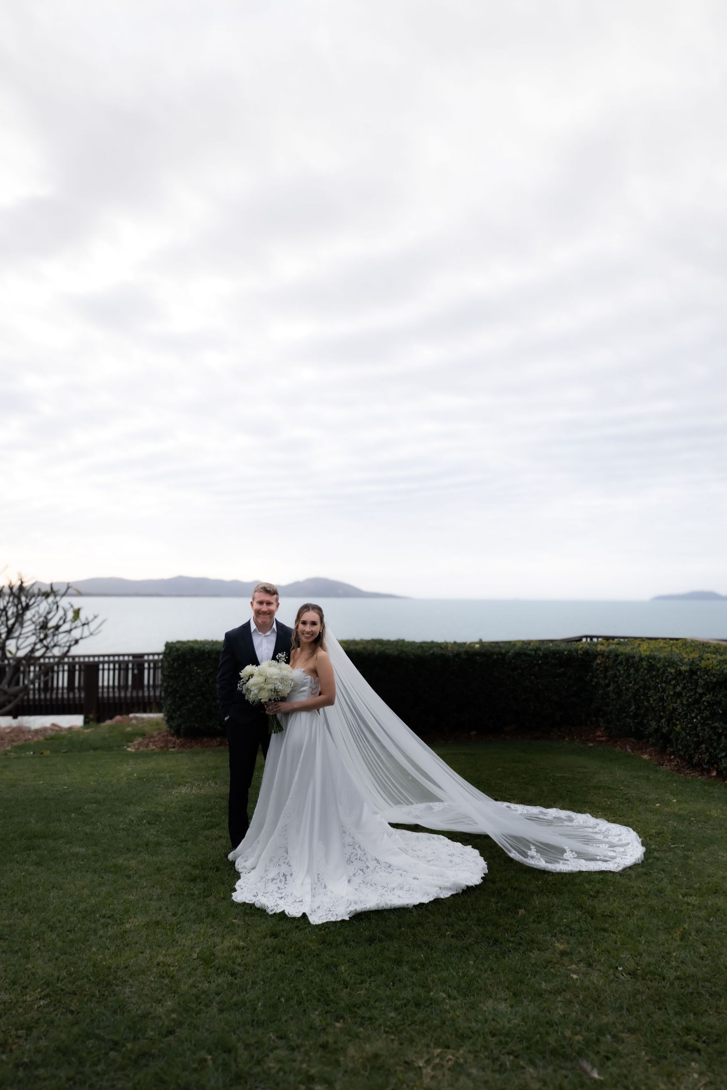 Dramatic wedding portraits with flowing veil against coastal landscape backdrop.