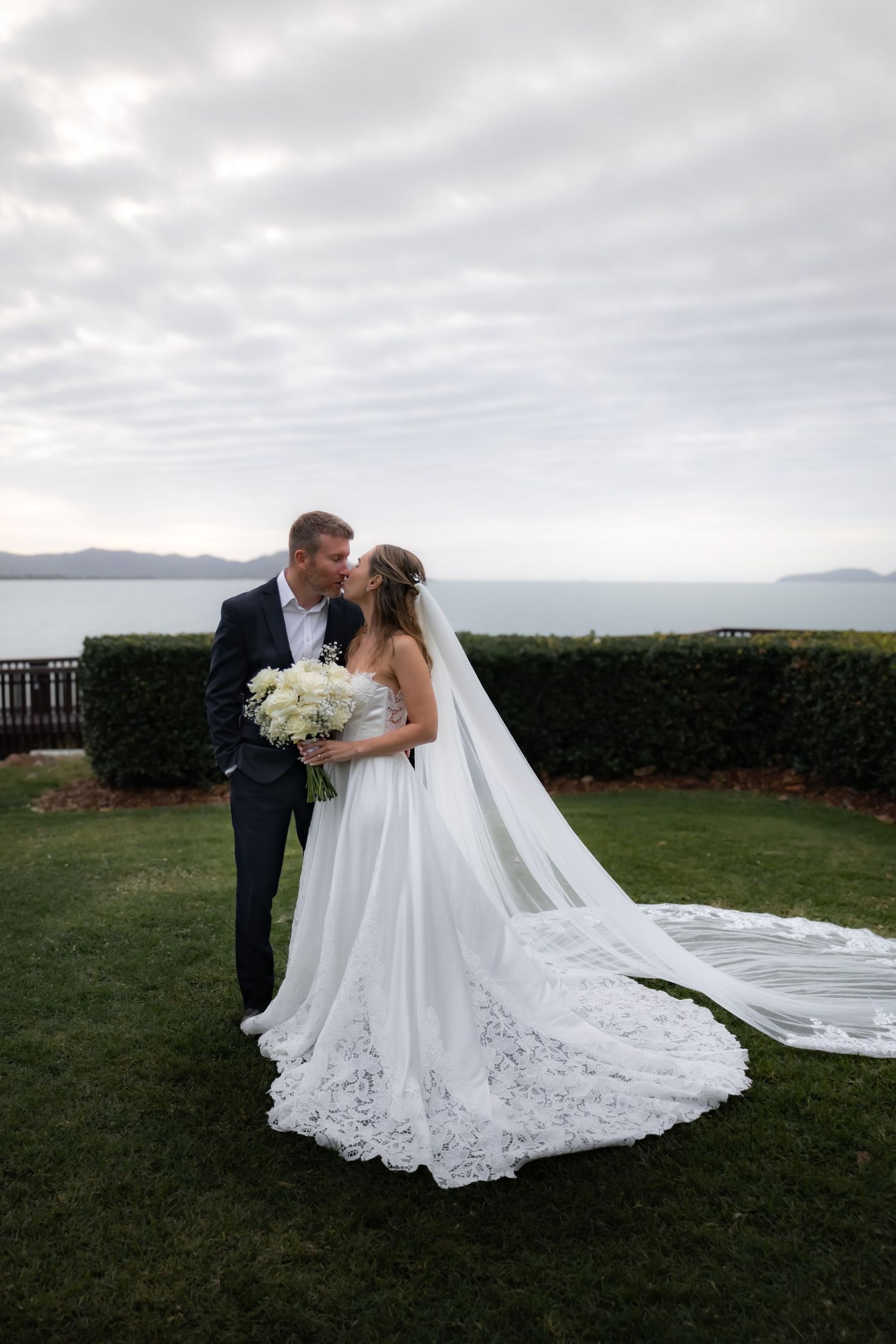 Elegant bridal portraits showcasing detailed lace dress and cathedral veil on oceanfront grounds.