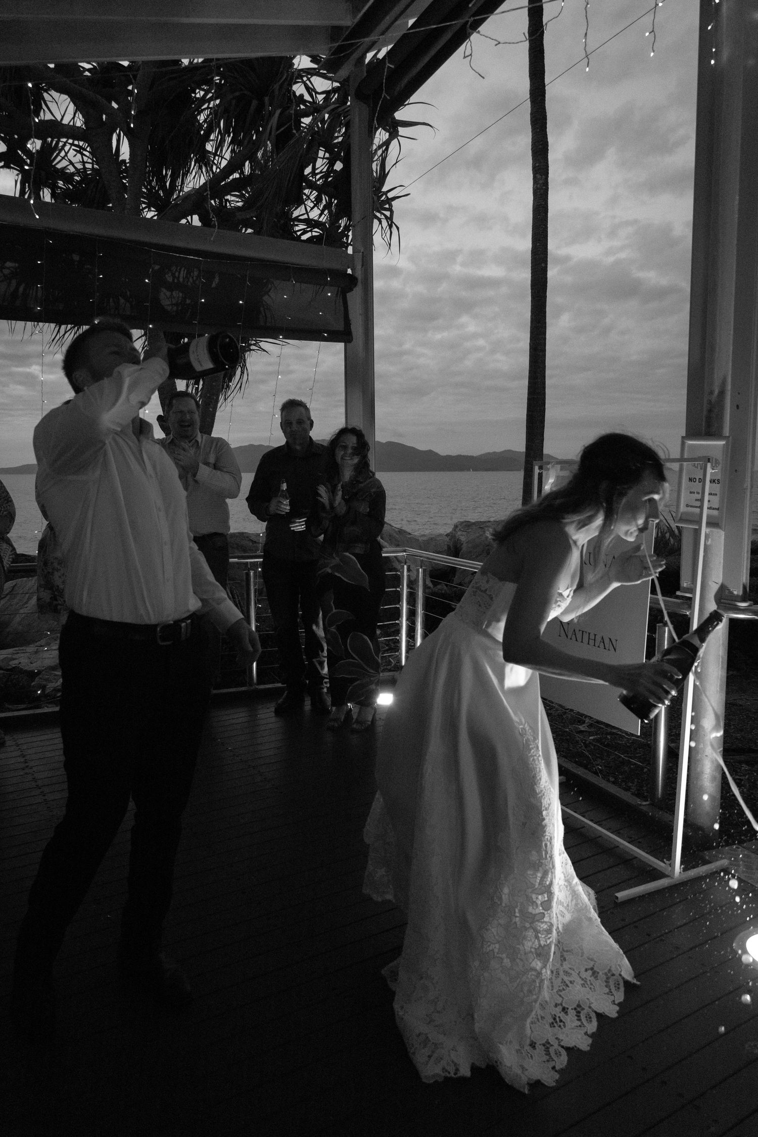Wedding reception celebration on a covered outdoor deck overlooking the water at sunset.