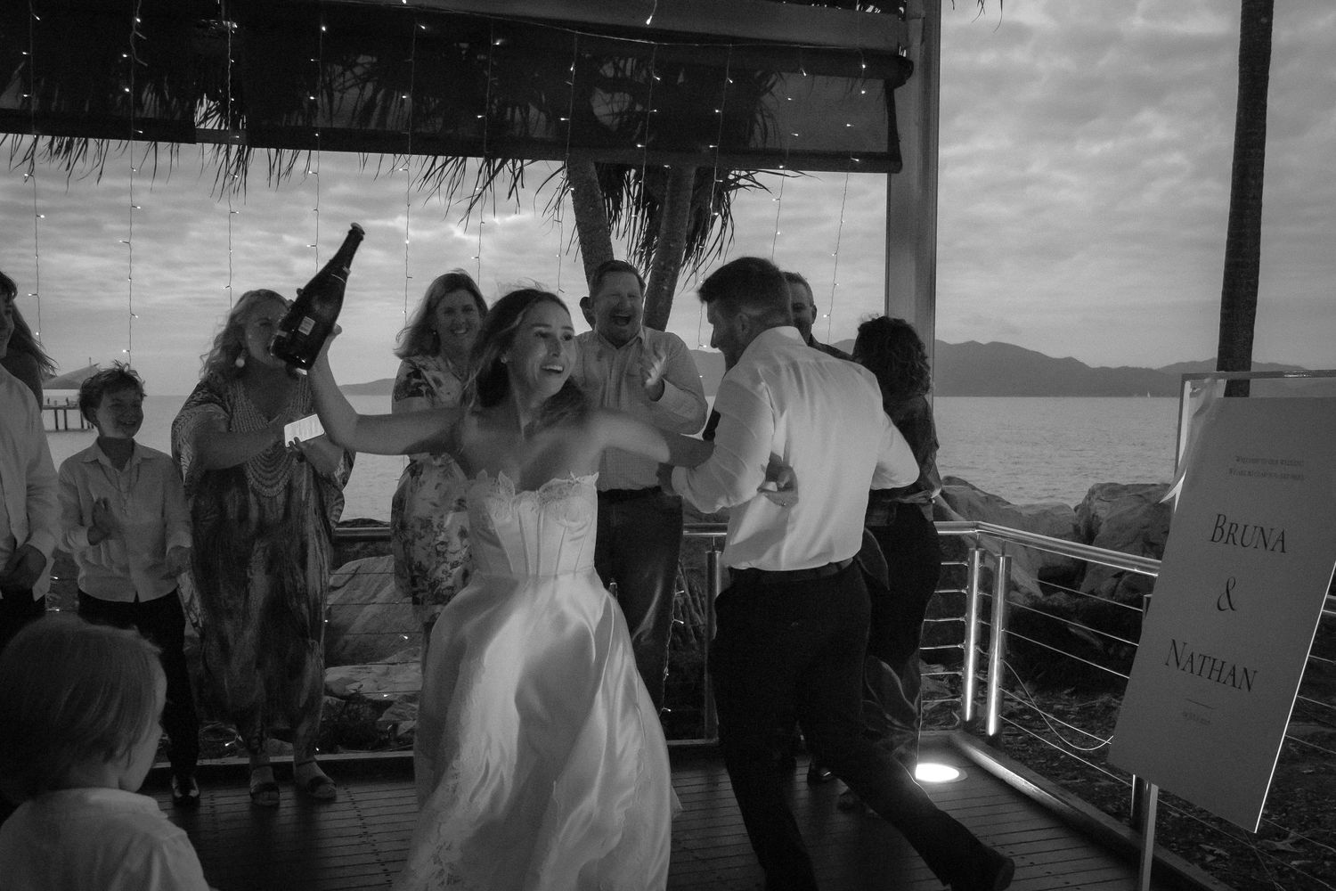 Wedding guests dance and celebrate at an outdoor reception venue with ocean views in the background.