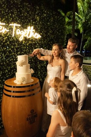 Wedding cake cutting celebration with guests gathered around a wooden barrel display.