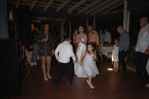 Wedding reception dance floor with guests celebrating under string lights and exposed beams.