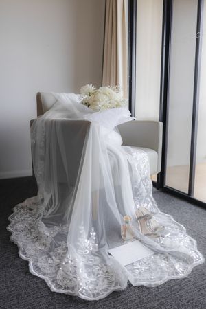 Elegant white lace wedding dress train laid out on grey carpet.
