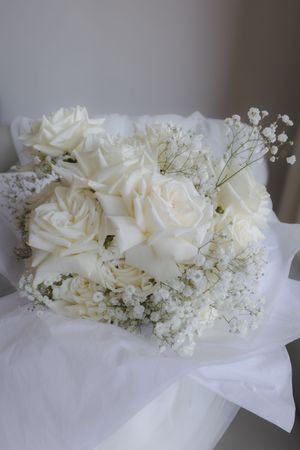 White roses and baby's breath floral arrangement on delicate white fabric.