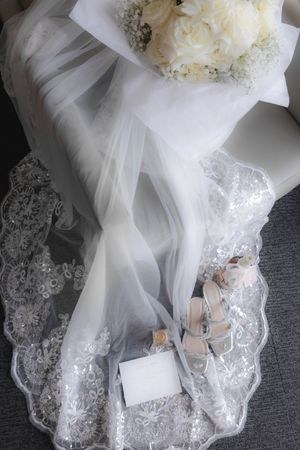 Wedding dress train with lace details and white floral accents on grey carpet.