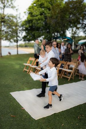Young attendees sitting on white aisle runner during outdoor wedding ceremony.