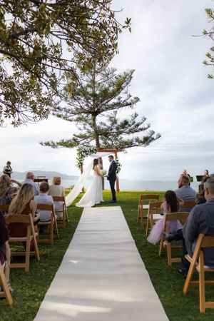 Wedding ceremony seating arrangement on grassy hillside with ocean backdrop.
