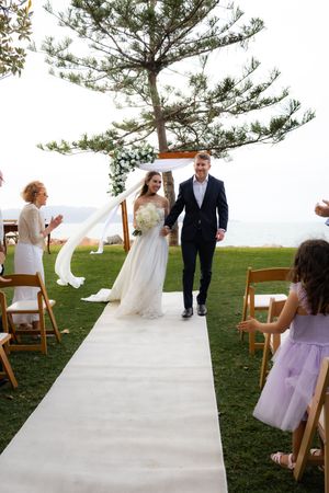 Wedding ceremony procession on white aisle runner with pine trees in background.