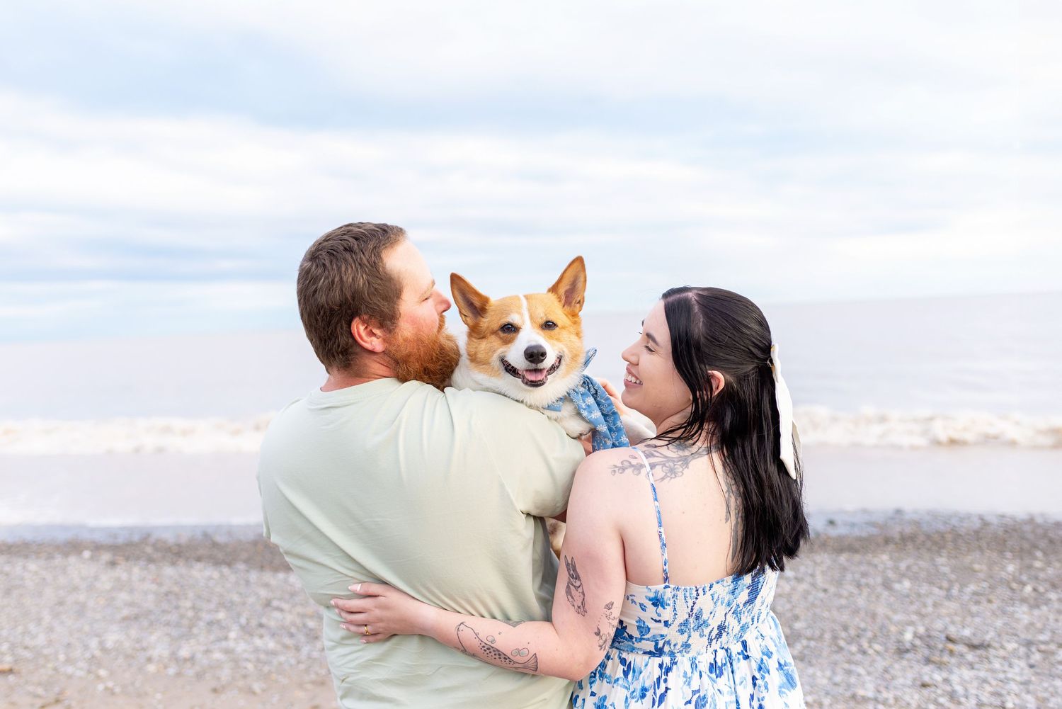 A couple holds their Corgi dog while enjoying a beach sunset together at Erie Rest.