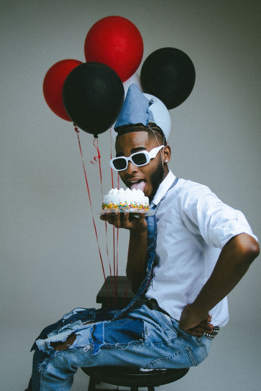 Person in white shirt and denim celebrates with red and black balloons in studio setting.