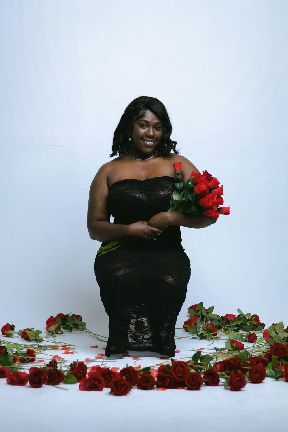 Glamour portrait with red roses arranged along white floor creating romantic setting.
