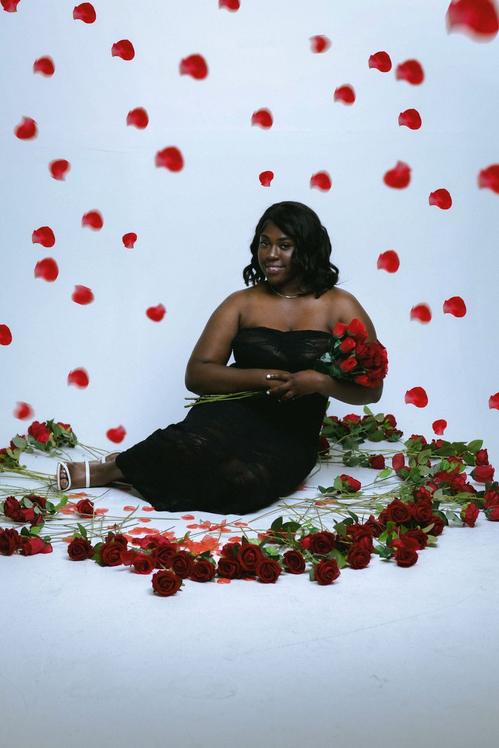 Elegant portrait session with scattered red rose petals creating romantic composition.