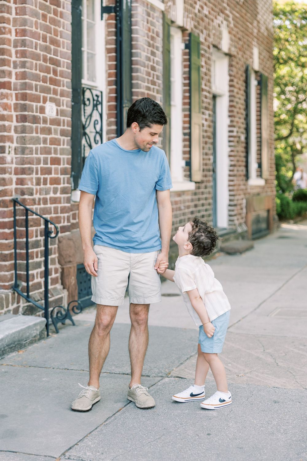Two people in coordinating blue and white outfits stand together on a brick sidewalk outside historic brick buildings.
