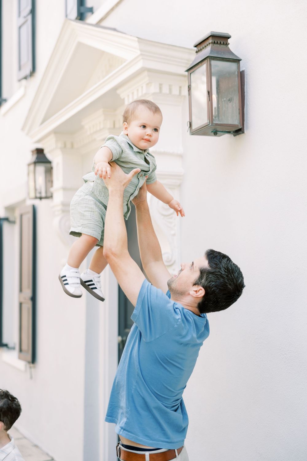 Playful sequence of a father in blue shirt lifting and playing with small child wearing gray outfit on white porch.