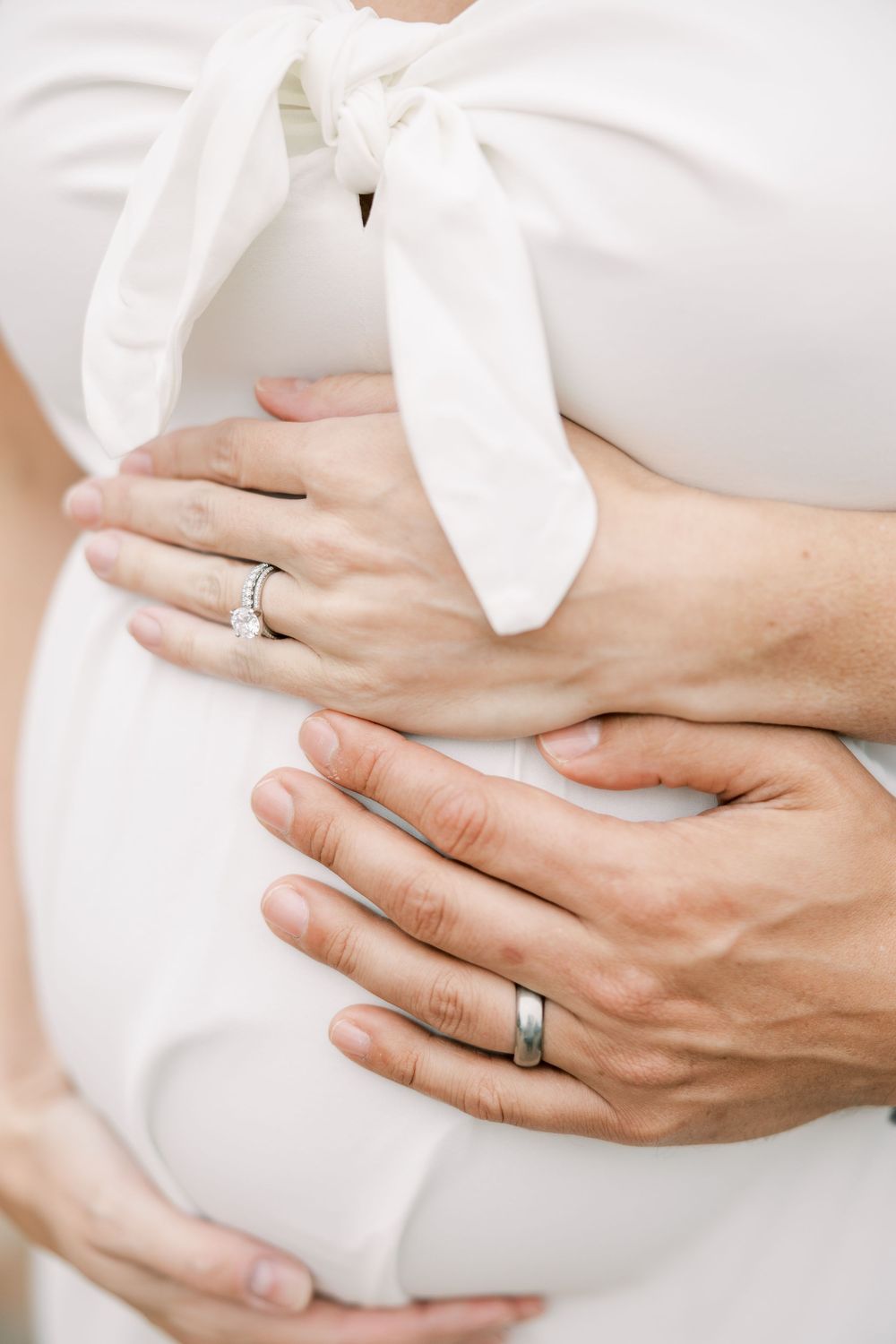 Close-up of hands wearing wedding rings resting on a white dress showing intimate tender moment.