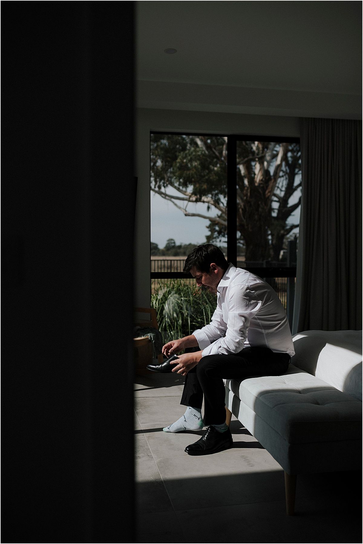 Moody silhouette of person sitting alone on white couch near window with dramatic lighting.