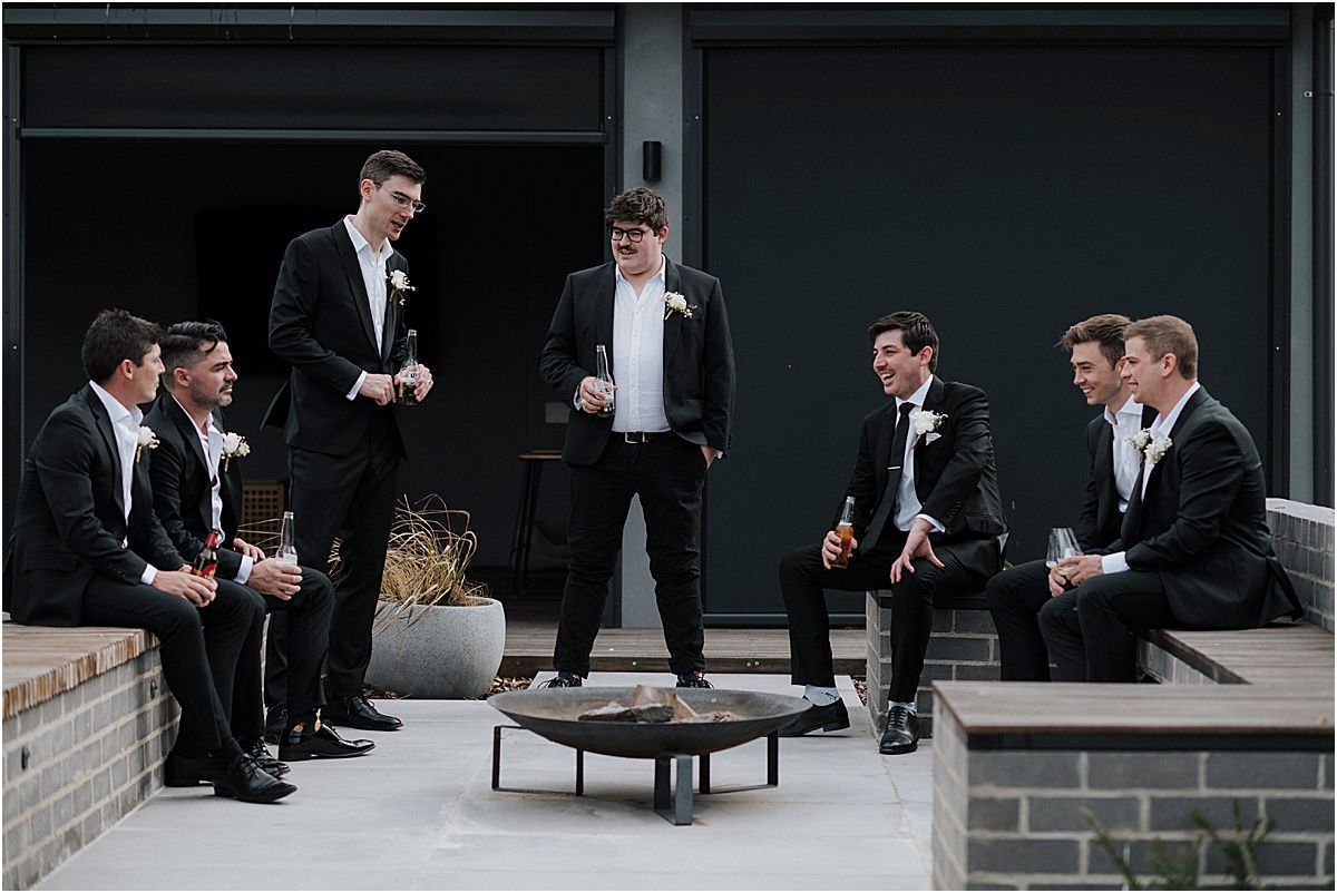 Groomsmen in formal attire gathered around a small table on an outdoor patio.