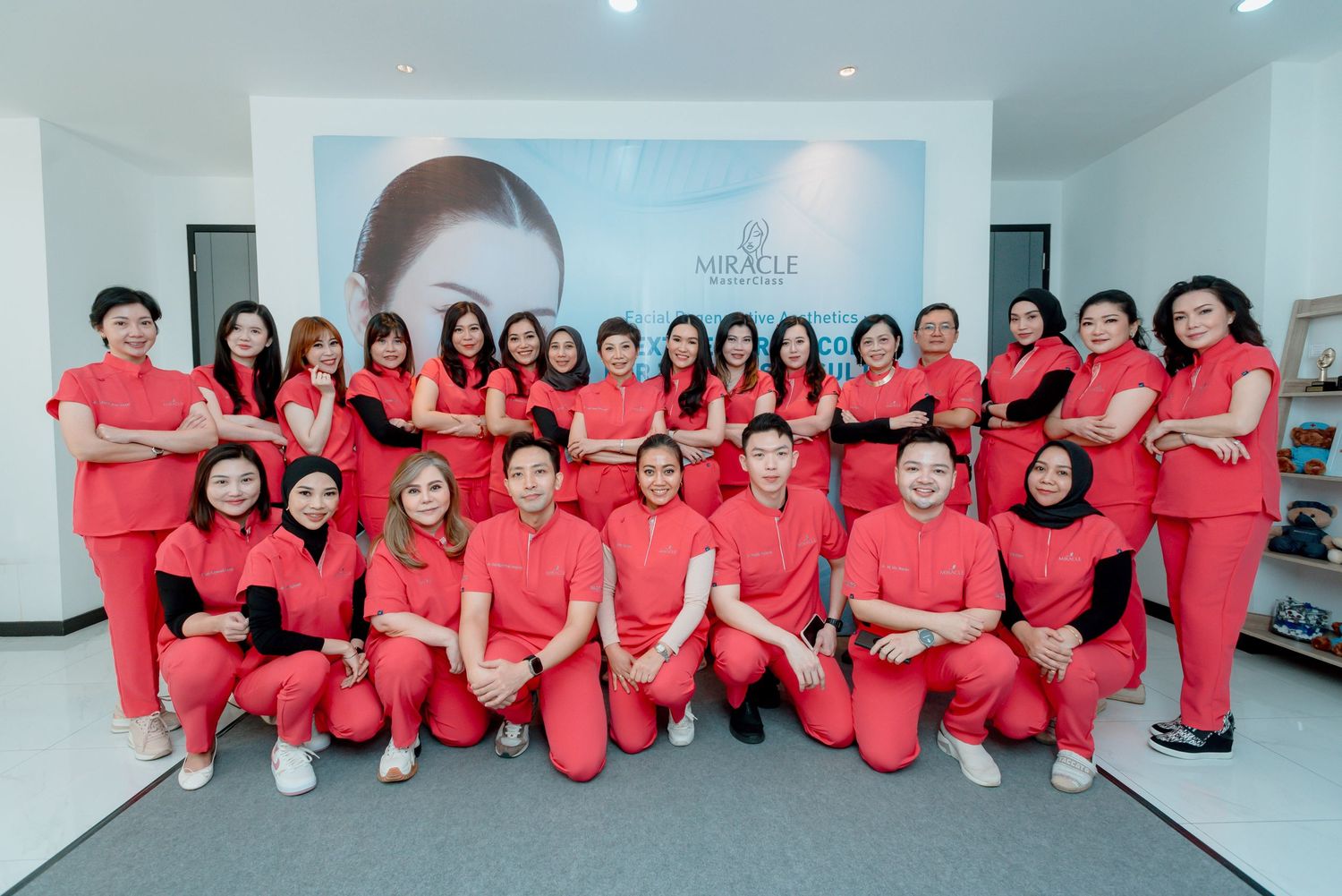 Group of healthcare workers in matching coral scrubs pose together in a medical facility hallway.